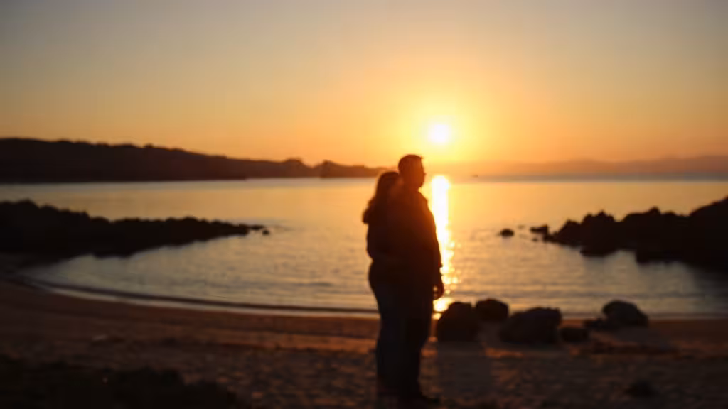 Coucher de soleil doré sur une baie côtière française, couple en silhouette contemplant la vue, ambiance escapade romantique